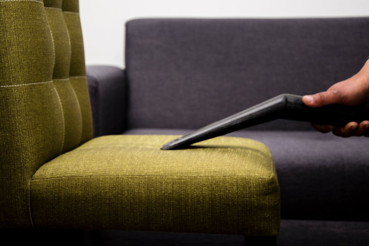 services-img Close-up of a person vacuuming a modern sofa chair indoors, highlighting cleaning service.